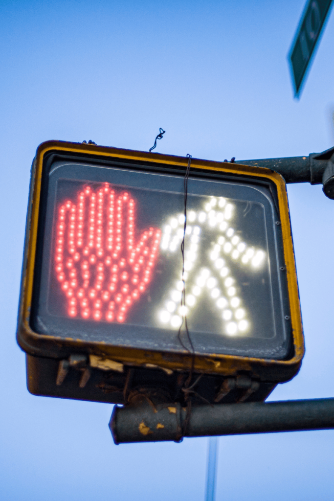 Reading signals. A street sign shows a red hand and a white person walking. Symbolizing stop and go