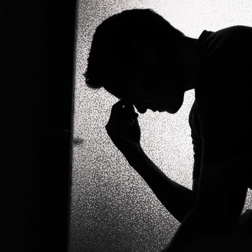 Black and white shot of a man's shadow. Hand to his face, sad
